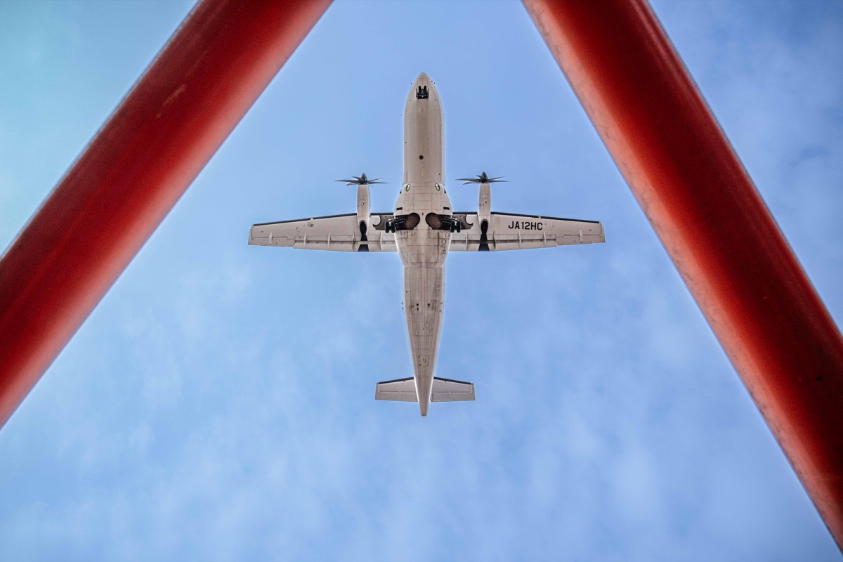 赤い誘導灯越しに見上げるプロペラ機